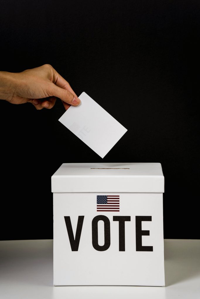 Close-up of a hand placing a ballot into a voting box marked 'Vote' with a USA flag.